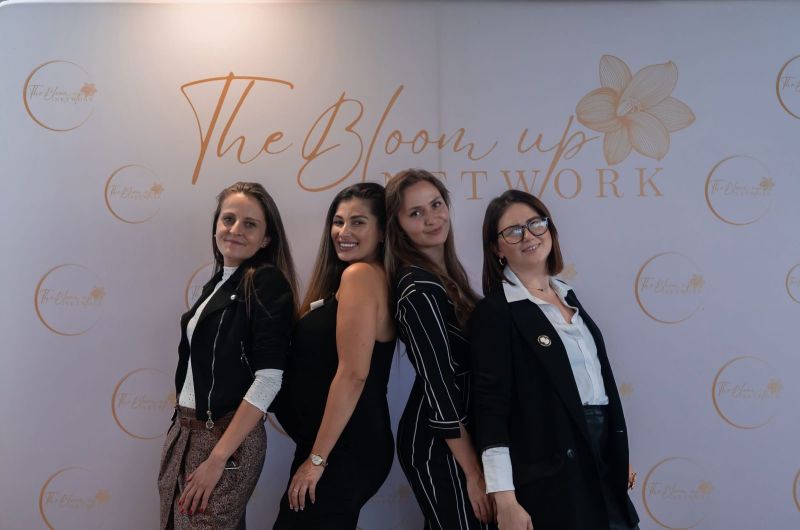 Cztery uśmiechnięte kobiety przy ściance z logo The Bloom Up Network